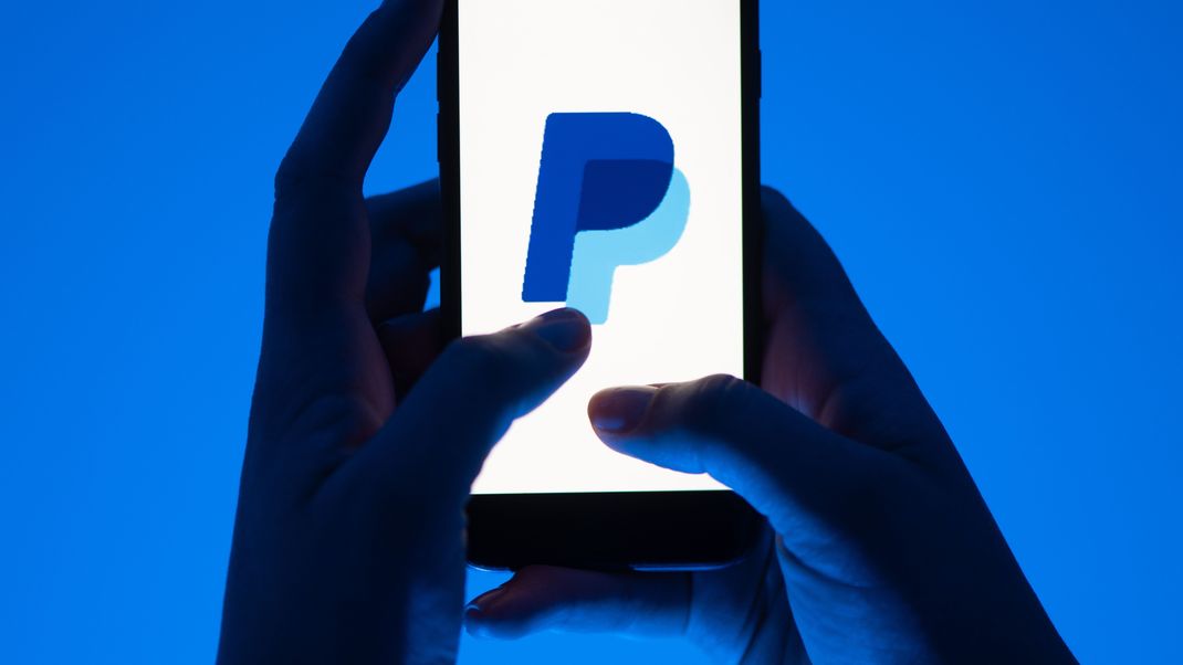 Eine Frau hält ein Smartphone mit dem Logo des Bezahldienst Paypal.