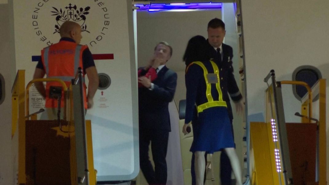 Frankreichs Präsident Macron bekommt kurz vor dem Verlassen des Flugzeugs die Hand seiner Frau Brigitte ins Gesicht.