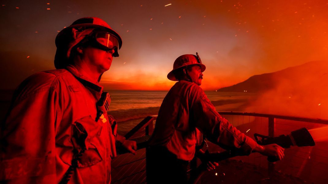 Feuerwehrleute stehen vor den lodernden Flammen an der Küste von Malibu.