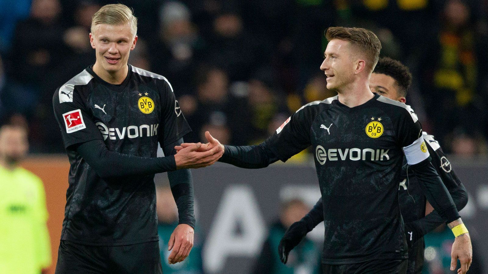 
                <strong>Ein historisches Bundesliga-Debüt</strong><br>
                Dieses Spiel wird so schnell wohl niemand vergessen. Der BVB gastierte in Augsburg, lag nach 55 Minuten mit 3:1 zurück. Alles sprach für einen Heimsieg. Und dann kam Haaland. Der damals 19-Jährige wurde nach dem 1:3 von Florian Niederlechner eingewechselt und machte sich bei den Fans innerhalb von 23 Minuten unsterblich: Haaland erzielte einen Dreierpack und drehte die Partie im Alleingang. Der BVB gewann am Ende mit 5:3. Drei Tore beim Bundesliga-Debüt? Dieses Kunststück gelang zuvor nur sechs anderen Profis – unter anderem Ex-Borusse Pierre-Emerick Aubameyang.
              