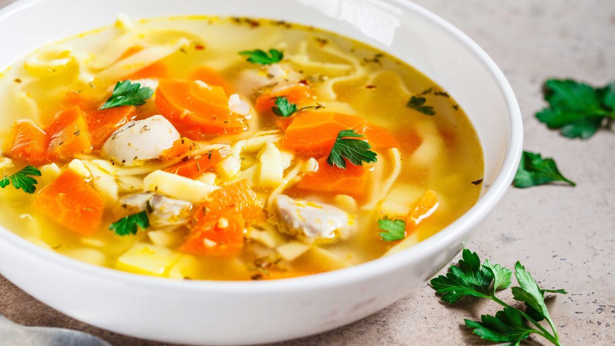 Chicken noodle soup with parsley and vegetables in a white plate.