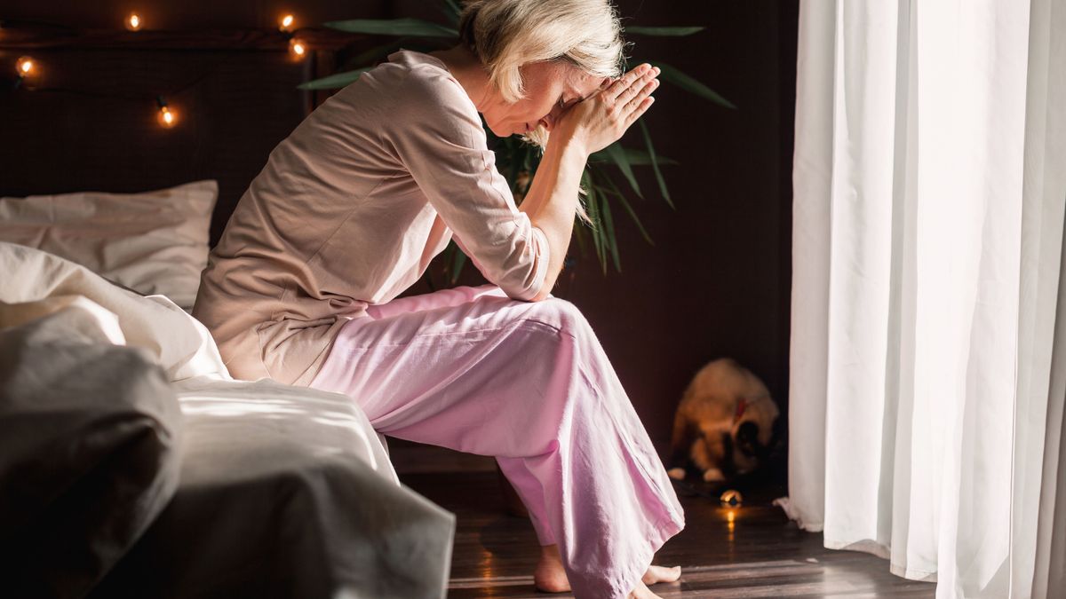 Unhappy sad middle aged woman sitting on bed at home