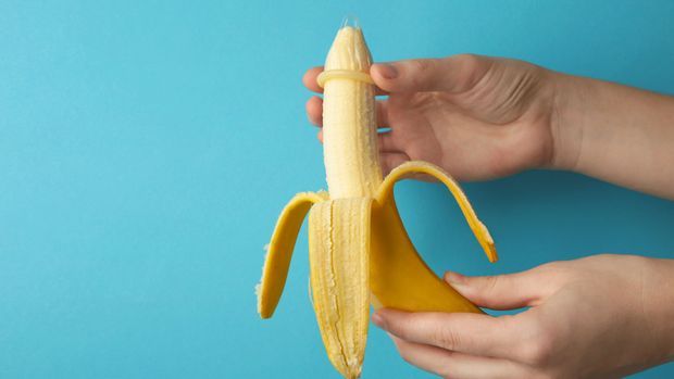 Female hand puts on a condom on a banana. Safe sex concept.