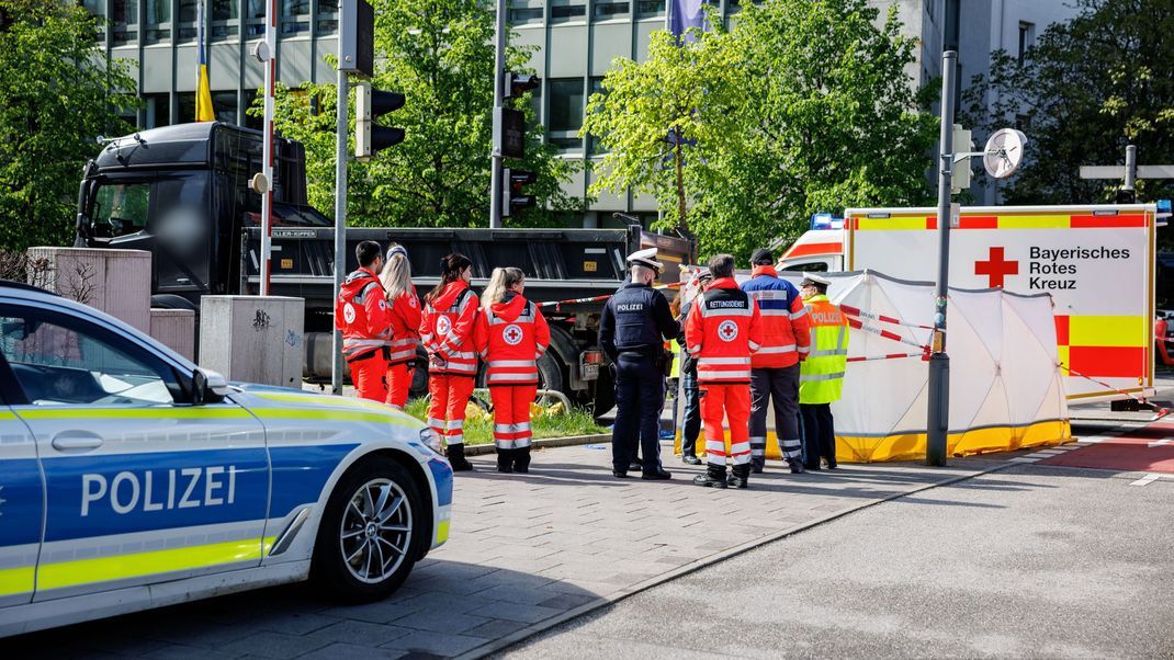 Rettungskräfte vom Bayerischen Roten Kreuz und Polizisten stehen an einer durch einen Sichtschutz abgeschirmten Unfallstelle am Effnerplatz. 