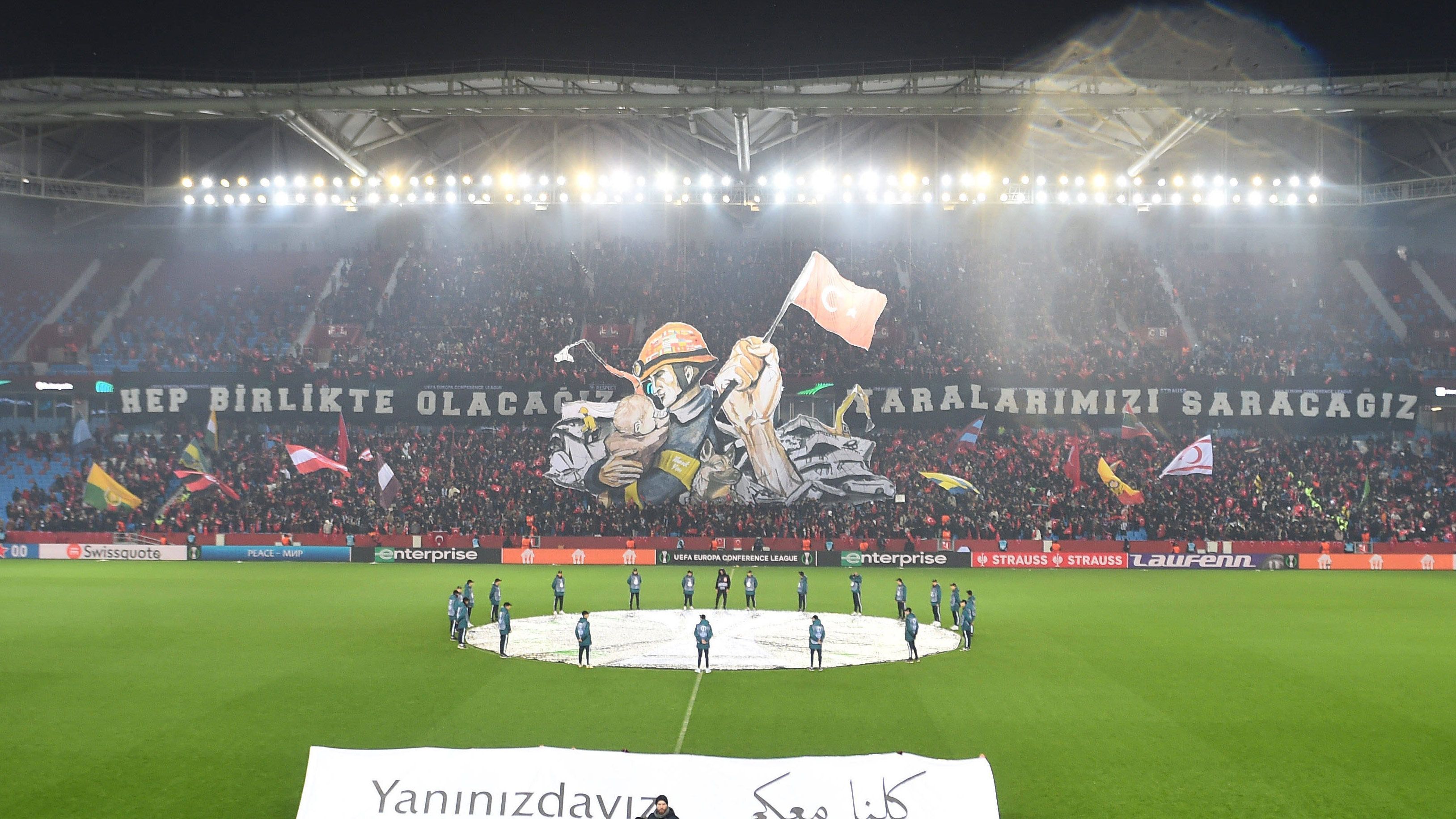 
                <strong>Trabzonspor - Fans gegen FC Basel mit emotionaler Choreo</strong><br>
                Beim K.-o.-Play-off-Hinspiel zwischen Trabzonspor und dem FC Basel kam es zu einer emotionalen Choreografie der türkischen Fans. Dabei wurde den Rettern nach dem schweren Erdbeben in der Türkei und in Syrien gedankt. Darauf zu sehen war eine Hilfskraft, die ein Kind in den Armen trägt. Auf dem Helm der Hilfskraft waren die Flaggen verschiedenster Nationen vertreten, die an den Hilfs-Aktionen beteiligt sind. Zudem war neben der Hilfskraft ein Arm zu sehen, der die türkische Flagge in der Hand hält. Außerdem wurde mit einem Spruchband unter anderem der Zusammenhalt hervorgehoben.
              