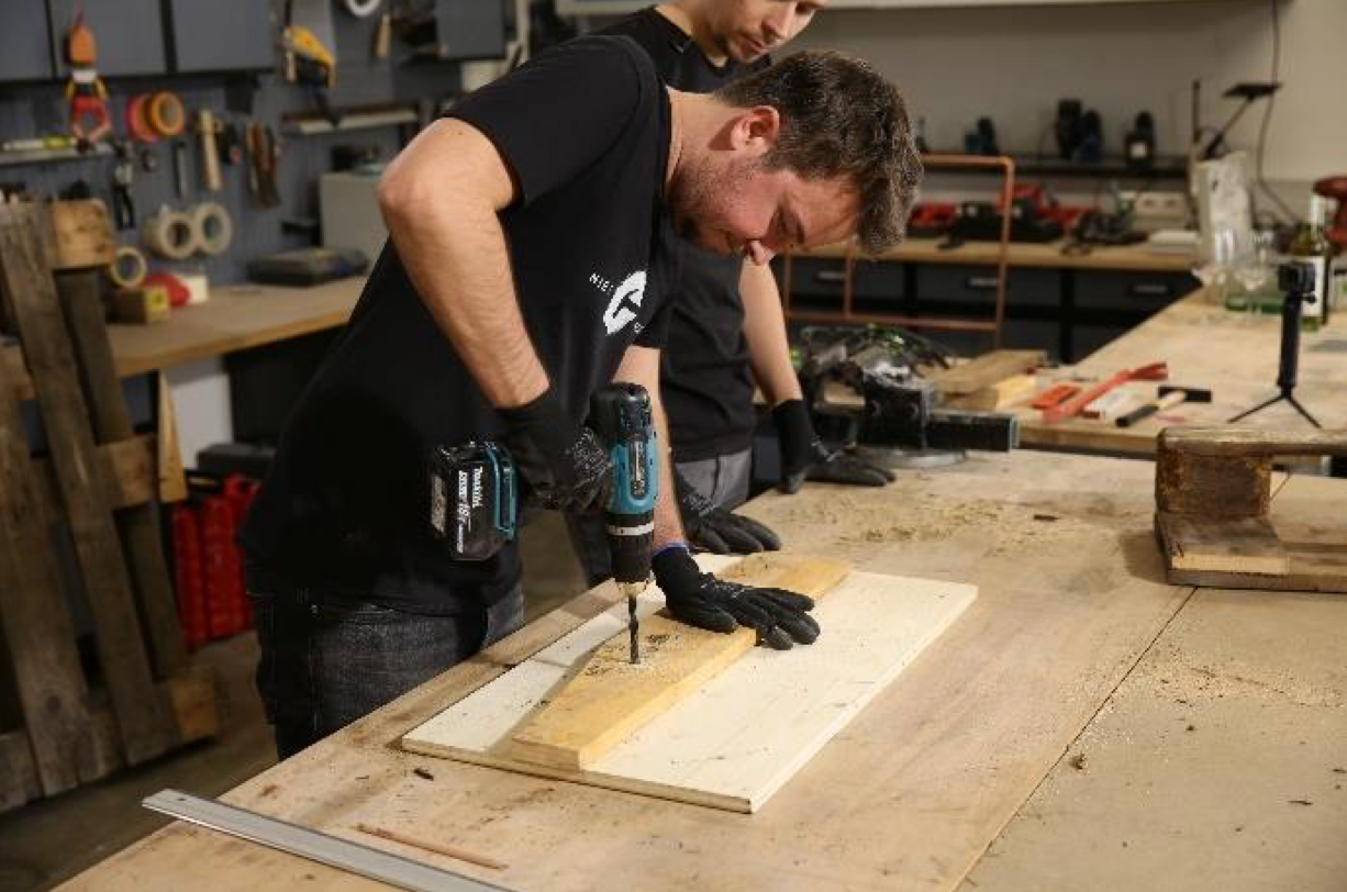 Für die Schlitze, in die die Weingläser gesteckt werden sollen, messen Sie den Durchmesser des Weinglasfußes und zeichnen die Maße in gleichmäßigen Abständen auf das lange Holzbrett. Daraufhin bohren Sie Löcher in die markierten Stellen mit einem Holzbohrer.