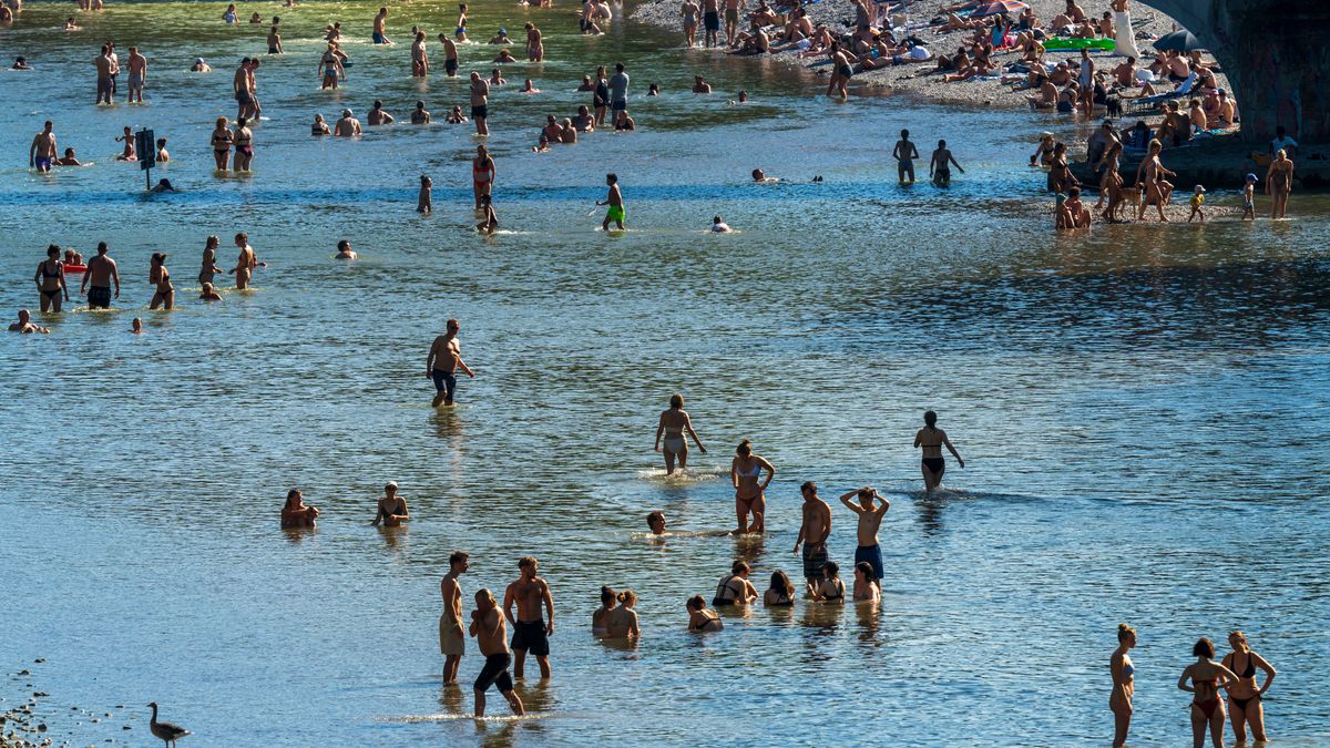 Badende genießen die Abkühlung im Wasser der Isar und auf den Kiesbänken rund um den Kabelsteg in München.