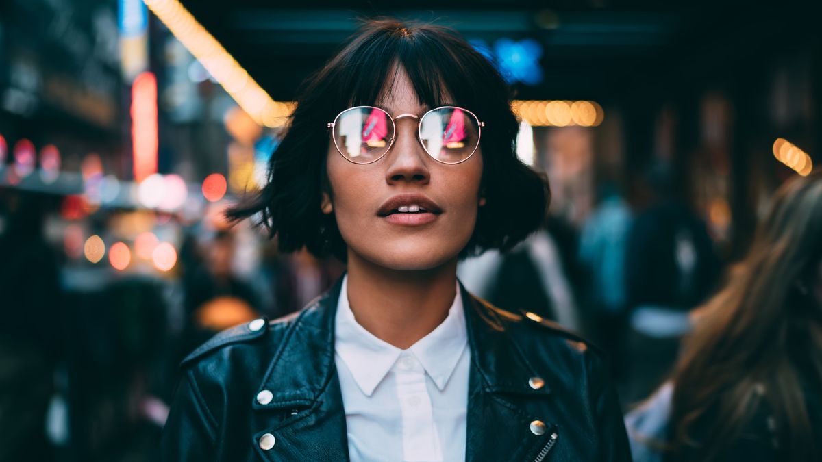 Caucasian woman in optical spectacles with neon reflection of lights standing at urbanity during travel vacations for visiting New York, attractive hipster girl in trendy apparel going out