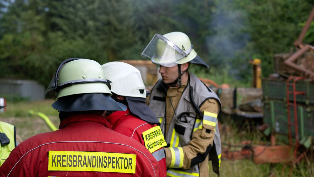 Einsatzkräfte der Feuerwehr stehen auf einem Gartengrundstück, aus dem Qualm aufsteigt. 