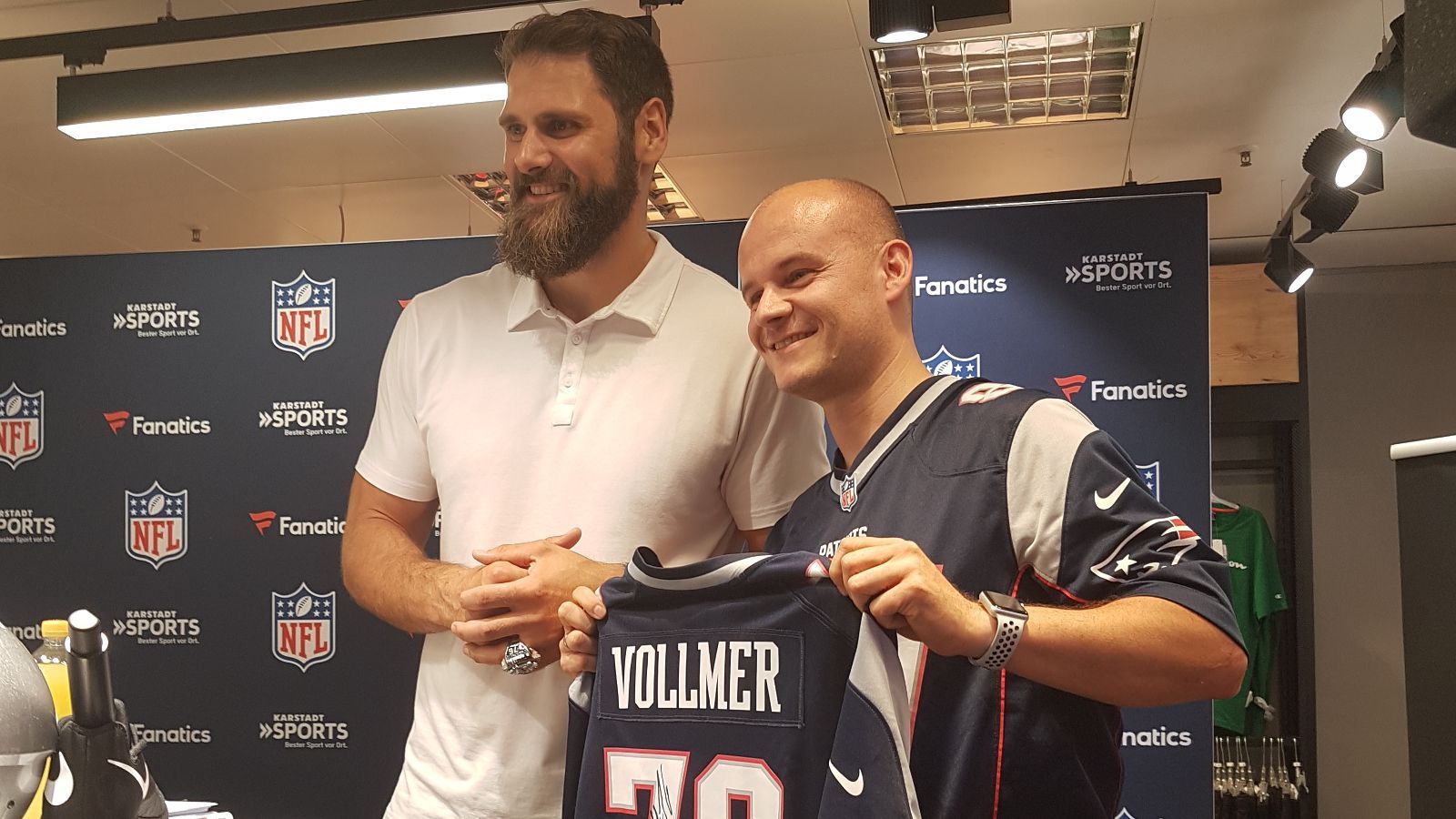 
                <strong>Deutsche NFL-Stars zur Autogramm-Stunde in München</strong><br>
                Dieser Fan kommt nicht nur in voller Patriots-Montur, sondern bringt auch ein Vollmer-Trikot zur Unterschrift mit. Vollmer selbst lebt immer noch in den USA, kommt aber gerne wieder nach Deutschland. "Amerika ist inzwischen meine Heimat geworden. Aber es ist immer super Familie und Freunde zu sehen. Inzwischen erkennen mich schon einige Leute auf der Straße, die Größe hilft natürlich nicht", scherzt der 2,03-Meter-Mann. "Aber es hält sich im Rahmen und das heißt ja auch, dass der Football hier immer beliebter wird, das ist toll", so Vollmer.
              