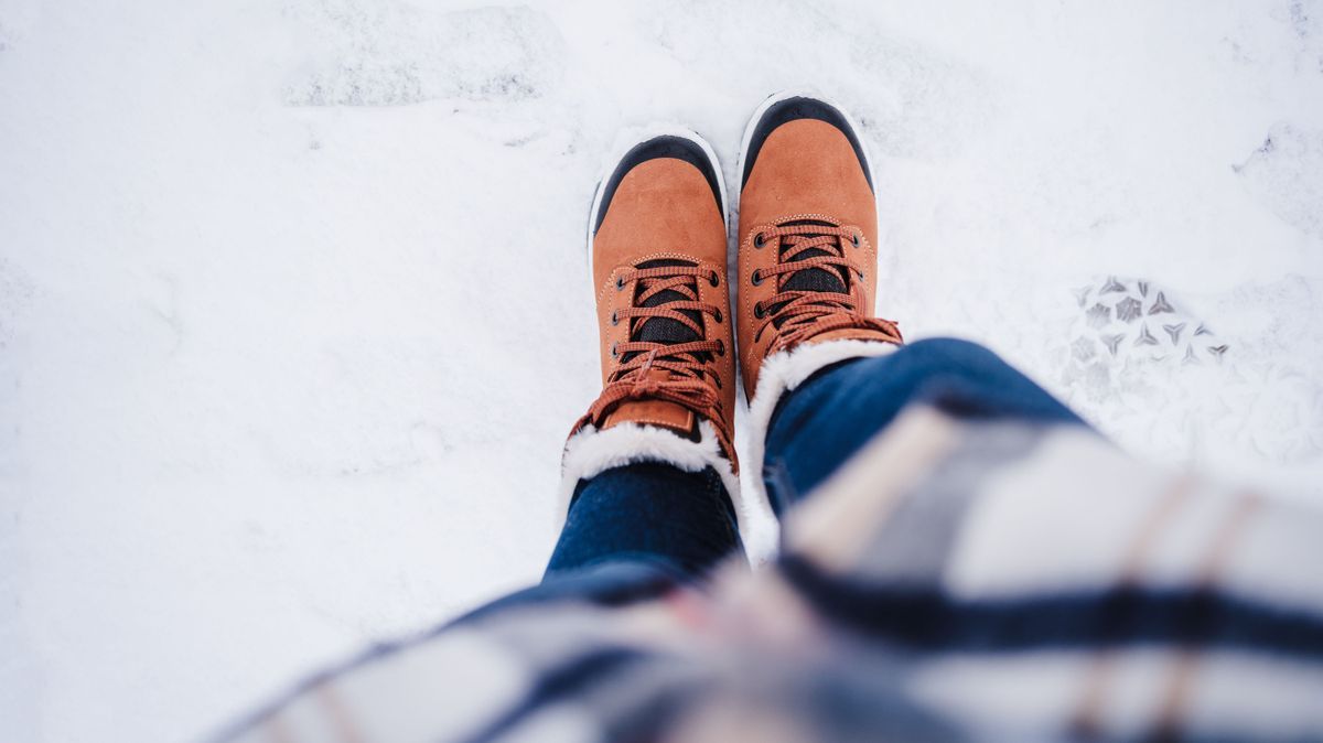 top view of unrecognizable female feet boots standing on snowy landscape during winter. hiking concept