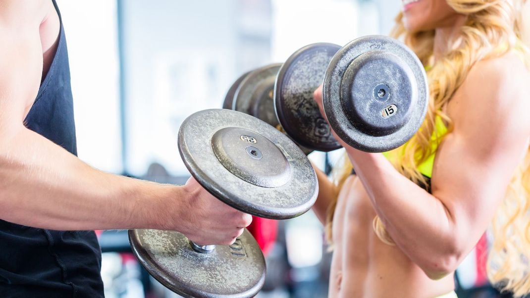 Man and woman in fitness gym lifting dumbbells looking at each other