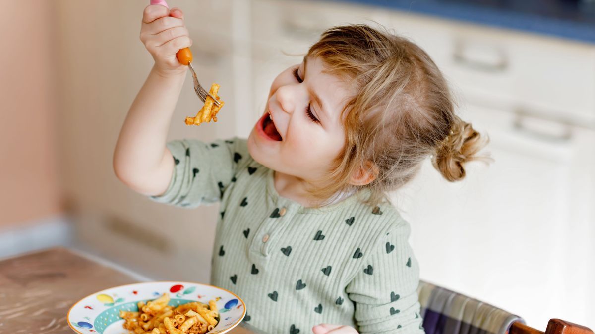 Adorable toddler girl eat pasta macaroni bolognese with minced meat. Happy child eating fresh cooked healthy meal with noodles and vegetables at home, indoors.
