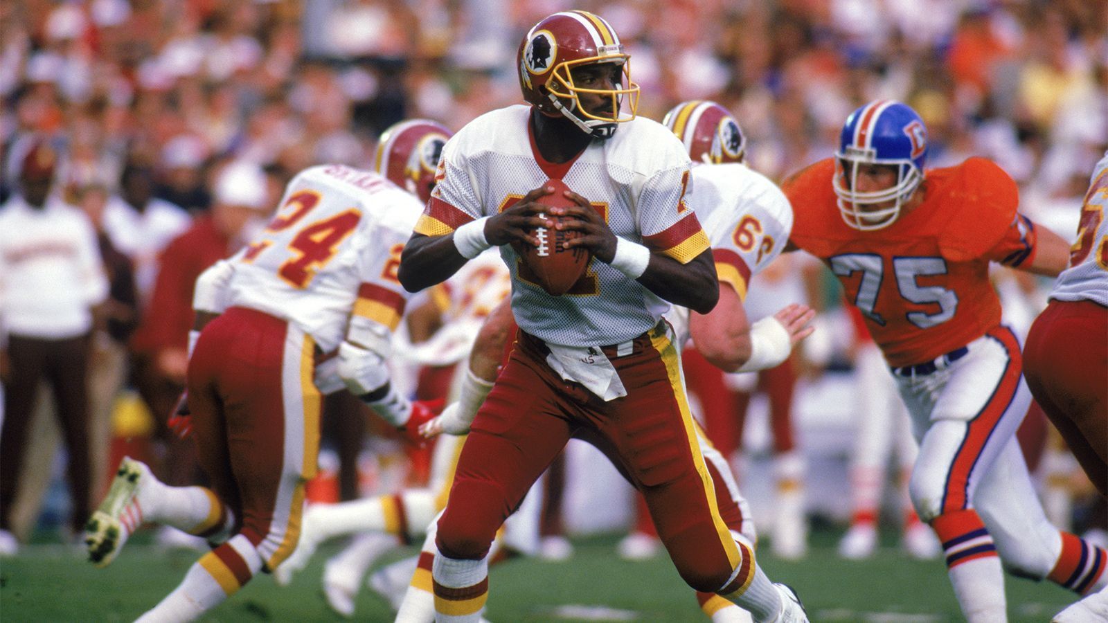 
                <strong>Doug Williams (Washington Redskins, Saison 1987)</strong><br>
                Williams wurde mit dem 17. Pick im Draft 1978 von den Bucs verpflichtet und startete insgesamt 67 Mal für Tampa Bay. 1986 unterschrieb er dann als Backup bei den Washington Redskins hinter Jay Schroeder. Ein Jahr darauf durfte er dann in zwei Spielen der Regular Season starten und erhielt auch in der Post Season das Vertrauen. Als erster afro-amerikanischer Quarterback gewann Williams dann in Super Bowl XXII (40-10 gegen die Denver Broncos) den Titel.
              