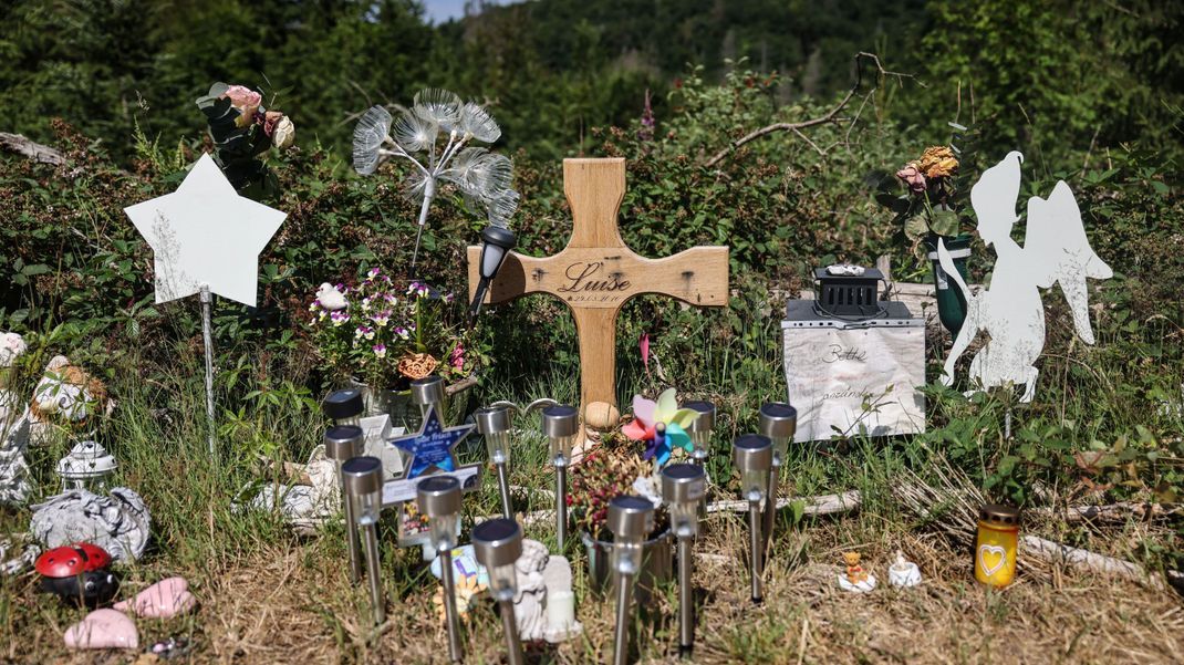 Ein Holzkreuz, Blumen und Lichter stehen am Waldrand an der Stelle, an der das Mädchen Luise tot gefunden wurde. 
