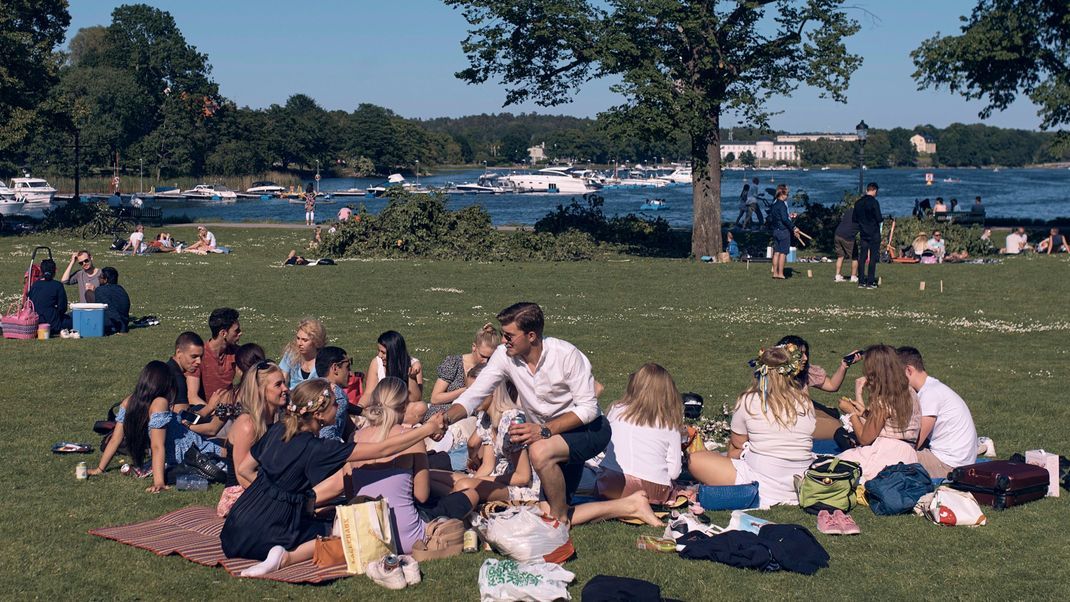 Schweden, Stockholm: Eine Gruppe junger Menschen picknickt während der jährlichen Mittsommer-Feierlichkeiten. In Skandinavien wird zur Sommersonnenwende das Mittsommer-Fest gefeiert.