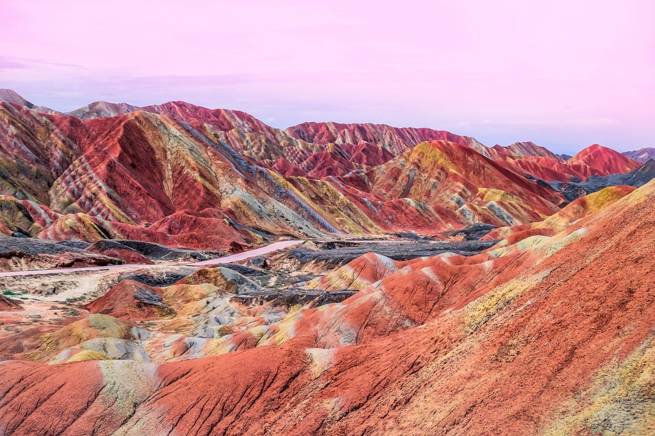Zhangye-Danxia-Geopark, China: Hier war kein:e Künstler:in am Werk, sondern die Erosion: Im Lauf von 24 Millionen Jahren formten Wind und Regen den roten Sandstein zu einer bunten Felslandschaft. Die kann man sich auf angelegten Wegen (näher) angucken.