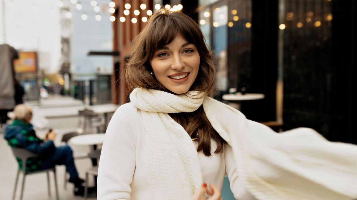 Excited lovely pretty girl with wonderful smile having outdoor on background of city cafe with lights. She is playing with her scarf and dancing 