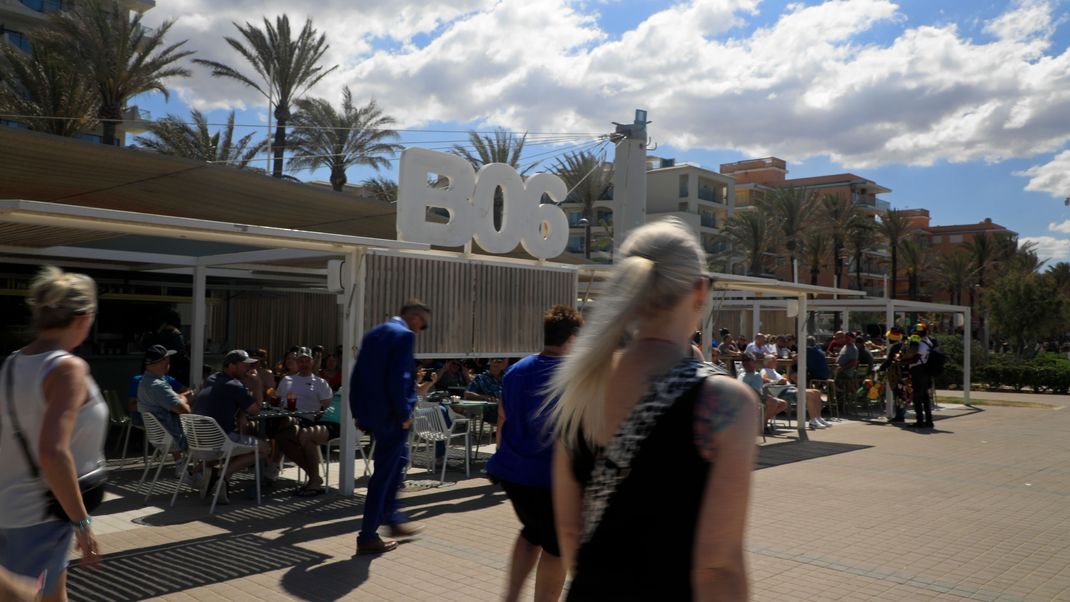 Menschen spazieren an einem sonnigen Tag am Ballermann 6 in Palma de Mallorca vorbei.