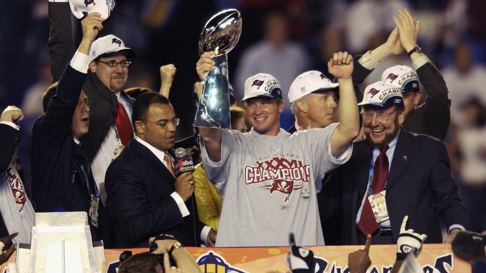 
                <strong>Super-Bowl-Sieg 2002 mit Head Coach Jon Gruden</strong><br>
                Im Jahr 2002, also 26 Jahre nach ihrer Gründung, landeten die Buccaneers sogar den ganz großen Coup und holten unter der Leitung von Head Coach Jon Gruden (Mitte) den Super Bowl. Heute coacht Gruden die Las Vegas Raiders - und will dort natürlich an die Erfolge von damals anknüpfen.
              