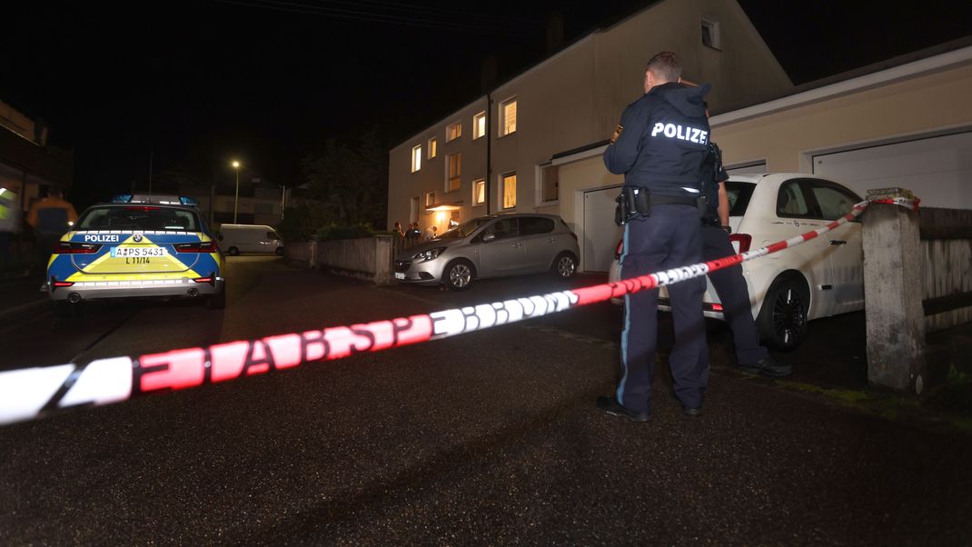 Polizisten stehen vor dem Mehrfamilienhaus, in dem drei Menschen erschossen wurden. 