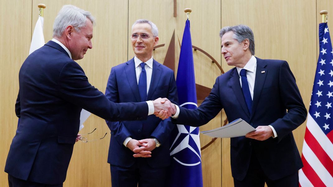 NATO-Generalsekretär Jens Stoltenberg (Mitte) schaut zu während sich Pekka Haavisto (links), Außenminister von Finnland, und Antony Blinken, Außenminister der USA, die Hand geben, nachdem die Beitrittsurkunde Finnlands überreicht wurde. 