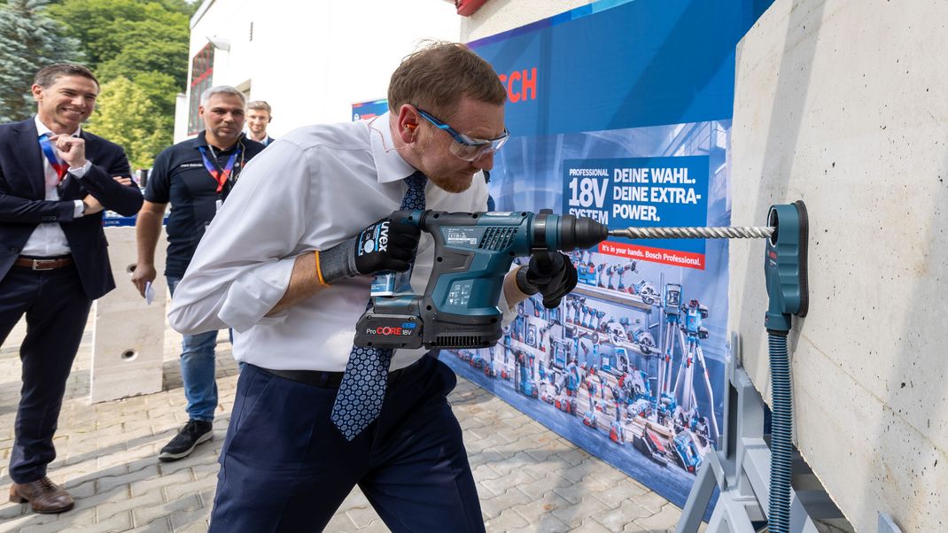 Sachsens Ministerpräsident Kretschmer bohrt mit einem Akku-Bohrhammer in einen Betonblock.