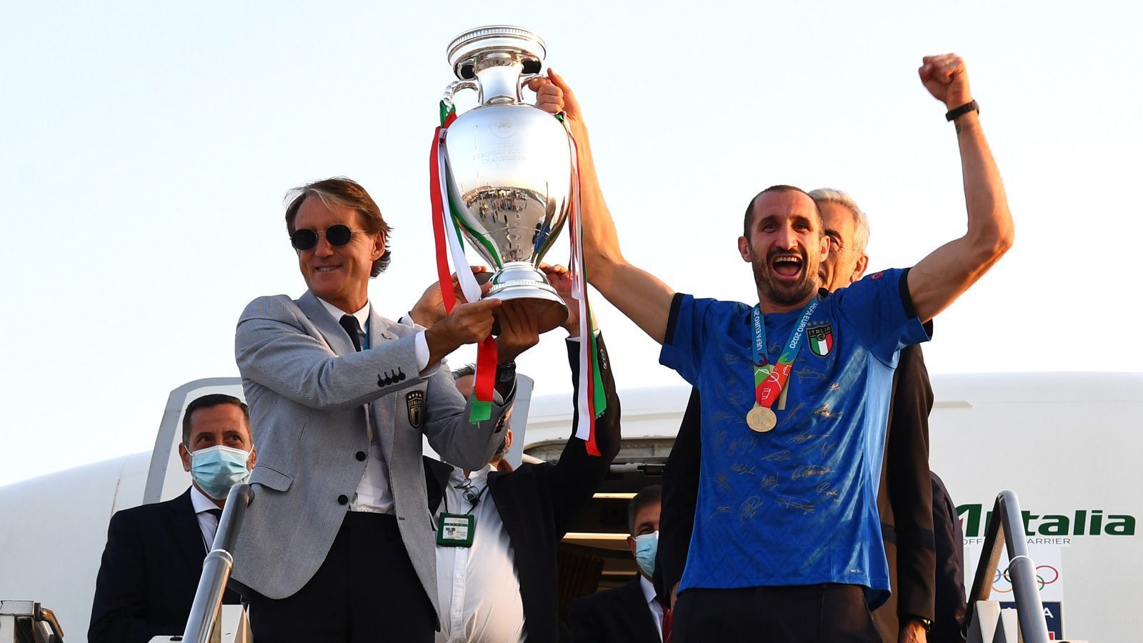 
                <strong>Chiellini zeigt den Pokal</strong><br>
                Trainer Roberto Mancini (l.) und Kapitän Roberto Chiellini tragen den Pokal aus dem Flugzeug. Die Laune ist ganz offensichtlich großartig.
              