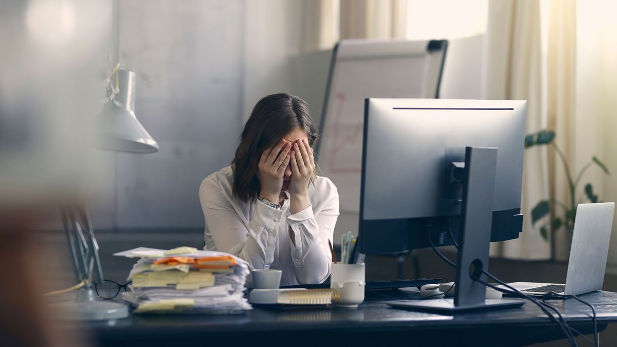 Frau am Schreibtisch, Kopf in den Händen vergraben. Burnout.