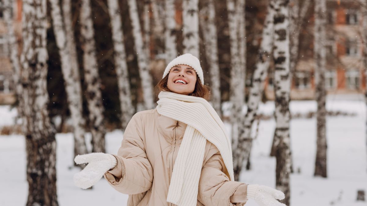 Happy smiling young woman portrait dressed coat scarf hat and mittens enjoys winter weather at birch winter park