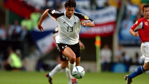 
                <strong>EM 2004 (Michael Ballack)</strong><br>
                EM 2004: Mit einem etwas bunteren Design in Schwarz-Rot-Gold treten Kapitän Michael Ballack und Co. bei der EM 2004 an - Wieder scheiden sie in der Gruppenphase aus. Dafür darf sich ein anderer Deutscher freuen: Otto Rehagel holt als Coach mit Griechenland den ersten und bislang einzigen EM-Titel für das Land.
              