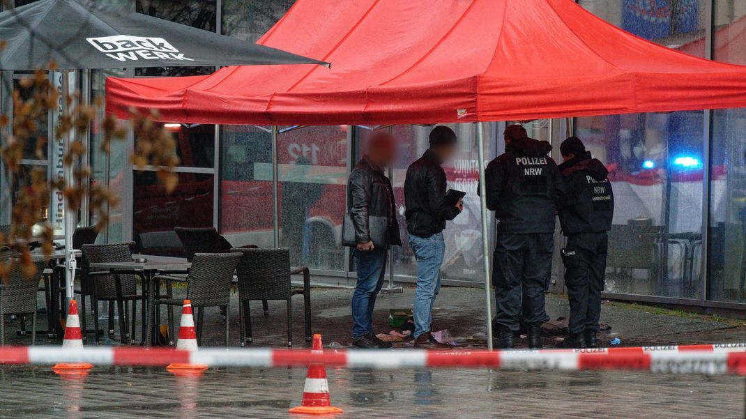 Polizeibeamte untersuchen unter einem Zeltdach den Tatort in der Innenstadt von Gummersbach.