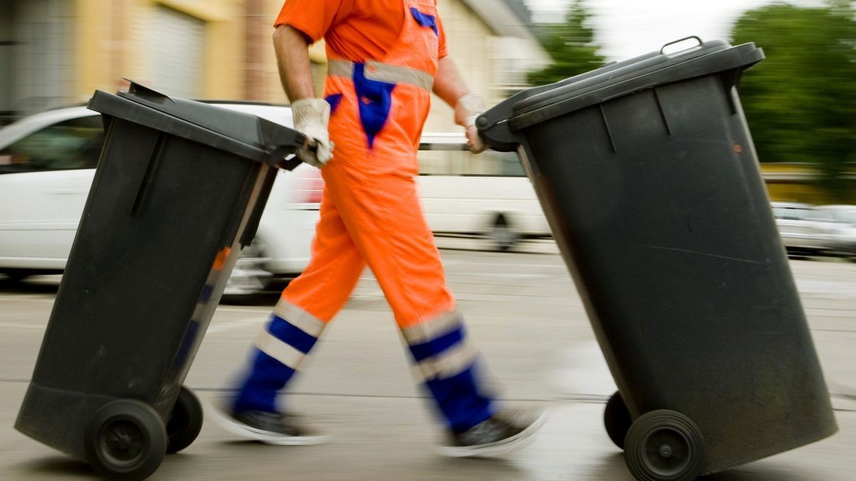 Ein Müllmann schiebt Mülltonnen