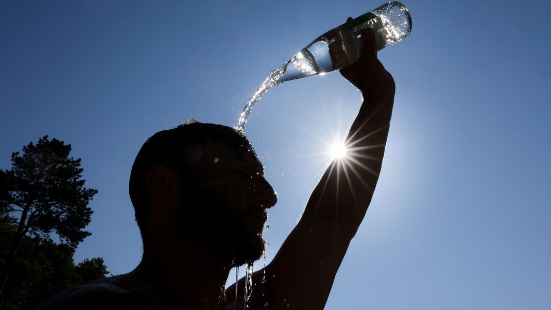 Ein Mann kühlt sich bei sommerlichen Temperaturen ab, in dem er sich eine Flasche mit Wasser über den Kopf schüttet.