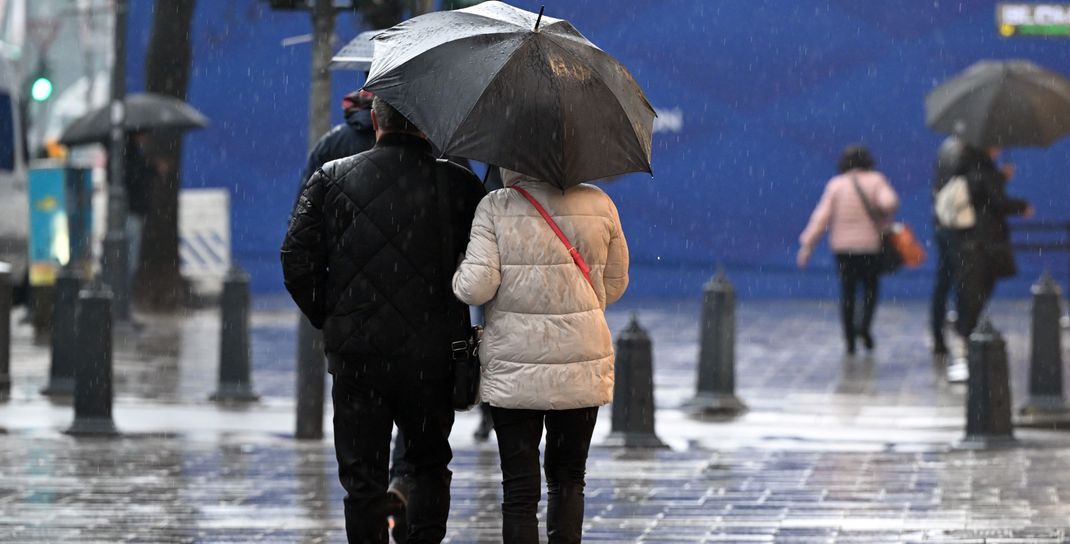 Passanten gehen unter ihrem Regenschirm über die Königsallee in Düsseldorf. 