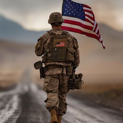 Soldier walks with US flag on road, under sky, in landscape