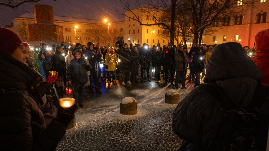 Männer und Frauen leuchten mit Taschenlampen, Smartphones, Lichterketten und anderen Leuchtmitteln am Geschwister-Scholl-Platz in München.