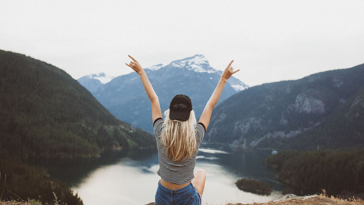 Behind shot of a young blond girl sitting on the cliff enjoying the view of the mountains and lake