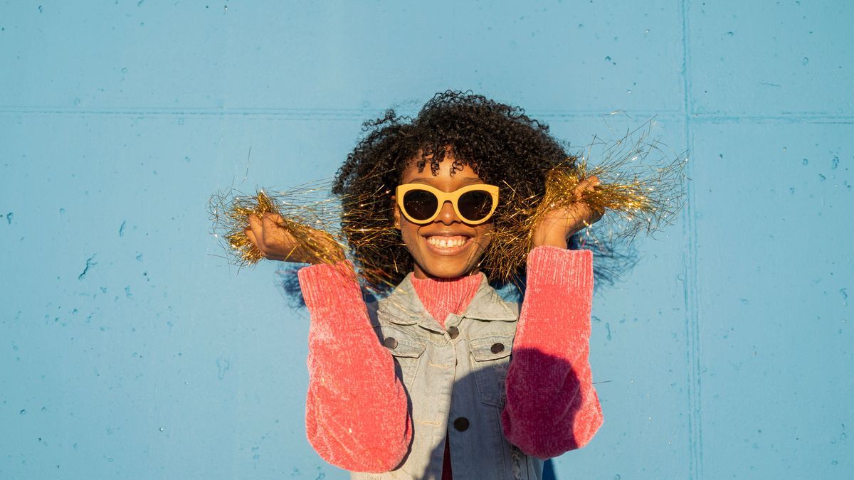 Happy woman holding golden tinsel in front of blue wall