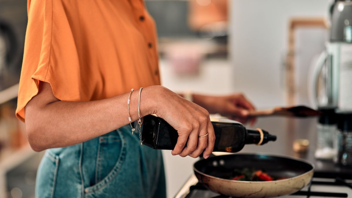 Hands, cooking and olive oil with a woman in the kitchen of her home for food or meal preparation. Stove, pan and container with a female chef in her house to cook for health, diet or nutrition