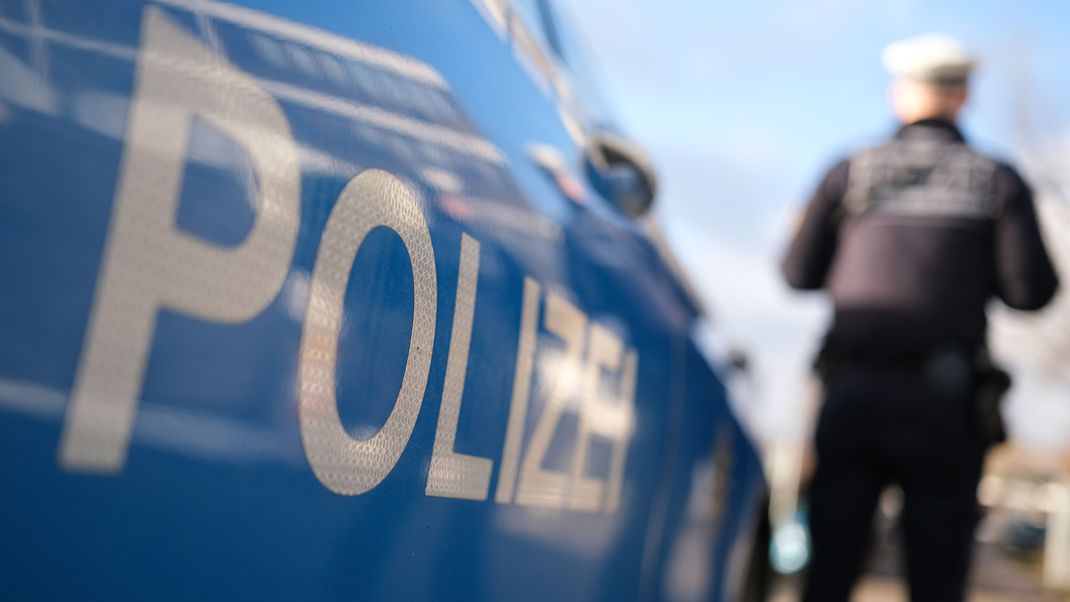 Ein Polizist steht vor einem Dienstfahrzeug (gestellte Szene).