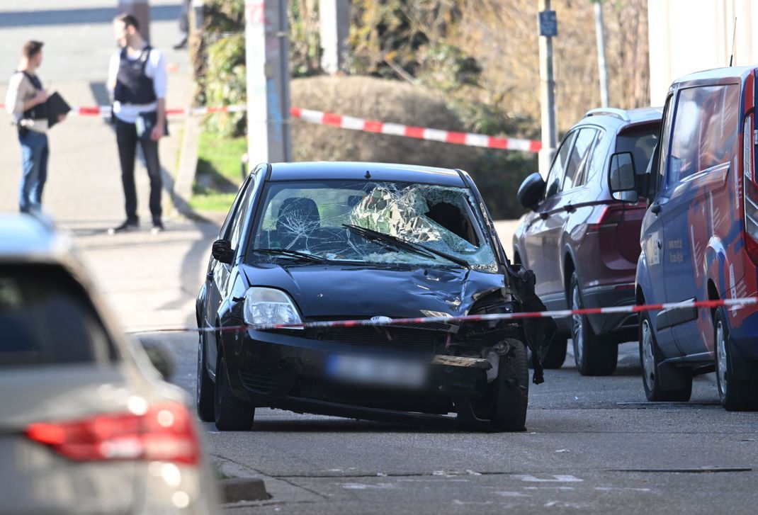 Beamte des Entschärfungsdienstes der Polizei sind an einem beschädigten Fahrzeug an einer Zufahrt zur Rheinbrücke im Einsatz.