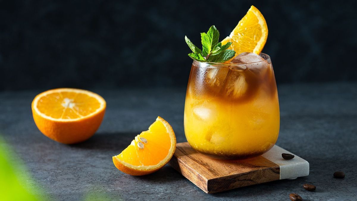 Bumble coffee with ice on a dark background. Espresso, orange juice and syrup in layers in a transparent glass with ice. Summer trendy refreshing coffee drink. Coffee house menu, recipe. Copy space