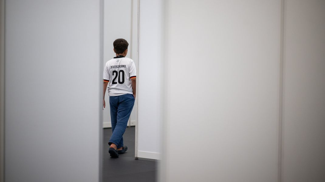 Ein neunjähriger Junge aus Syrien mit Deutschland-Trikot geht im Ankunftszentrum am ehemaligen Berliner Flughafen Tegel durch einen Gang.