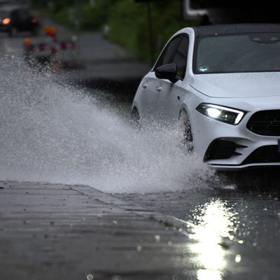 Ein Auto fährt durch eine große Wasserlache auf der Fahrbahn in Köln.