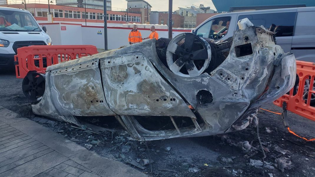 Großbritannien, Sunderland: Das Bild zeigt ein ausgebranntes Auto in Sunderland, während Anwohner mit Aufräumarbeiten beginnen. 