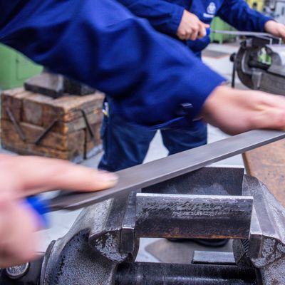 Lehrlinge arbeiten mit der Metallfeile an Schraubstöcken in einer Lehrwerkstatt.