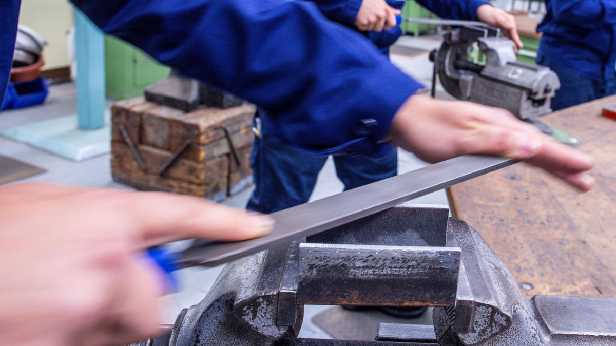 Lehrlinge arbeiten mit der Metallfeile an Schraubstöcken in einer Lehrwerkstatt.