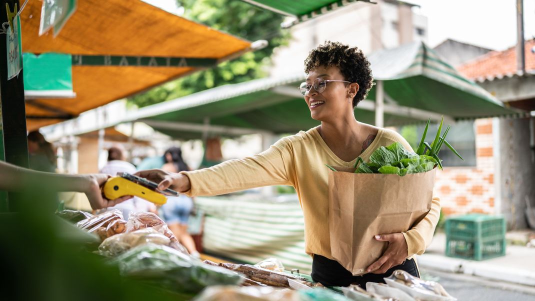 Young woman paying with mobile phone at a street market