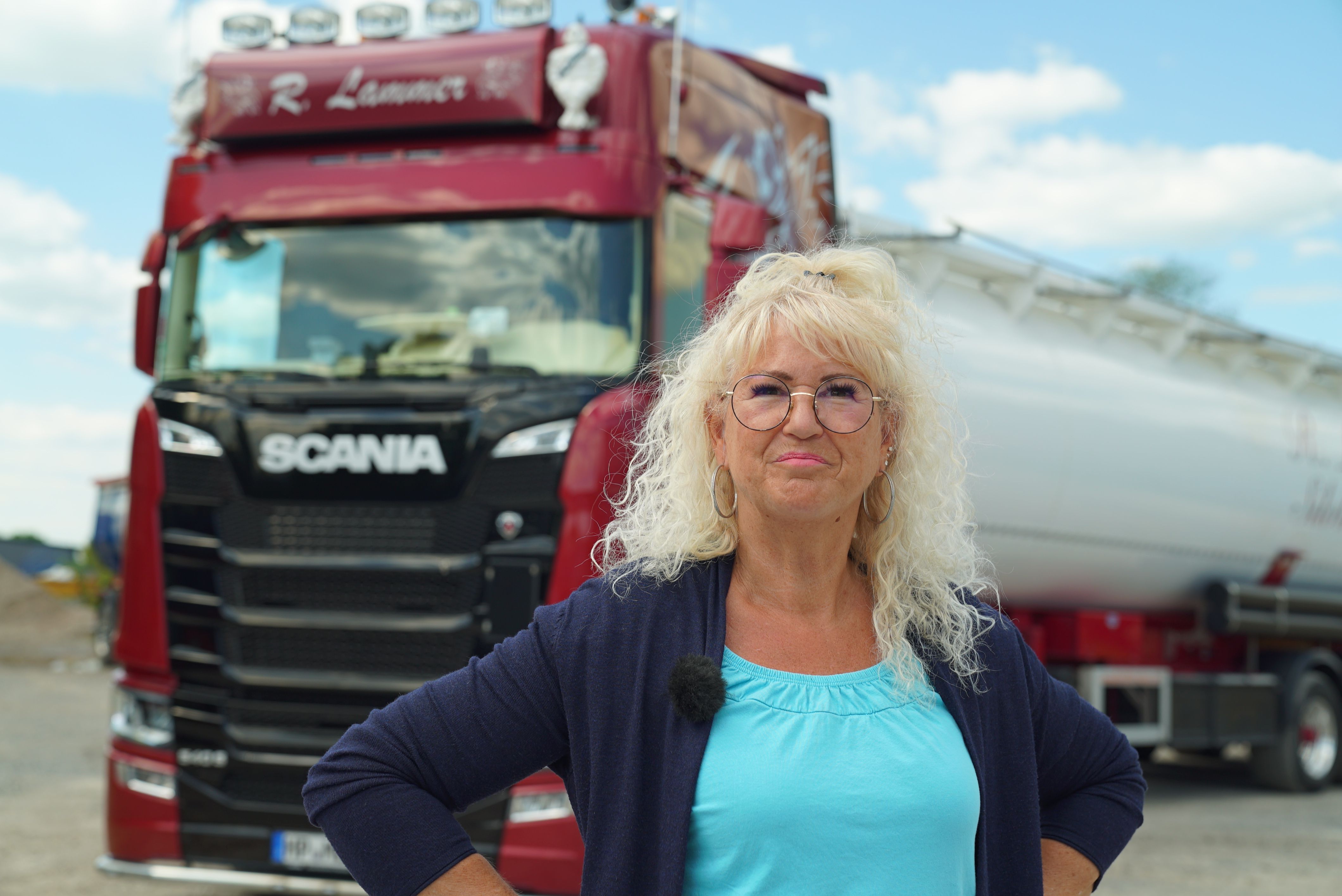 "Truckerbabe" und Schlagerfan Bettina steht vor ihrem roten Truck und posiert in Richtung Kamera.